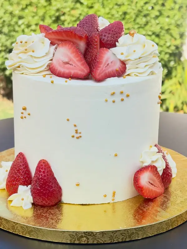 Torta blanca con frutillas frescas, crema y perlas doradas