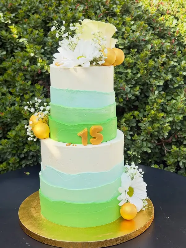 Torta de tres pisos en degradé verde con flores blancas y número 15 dorado